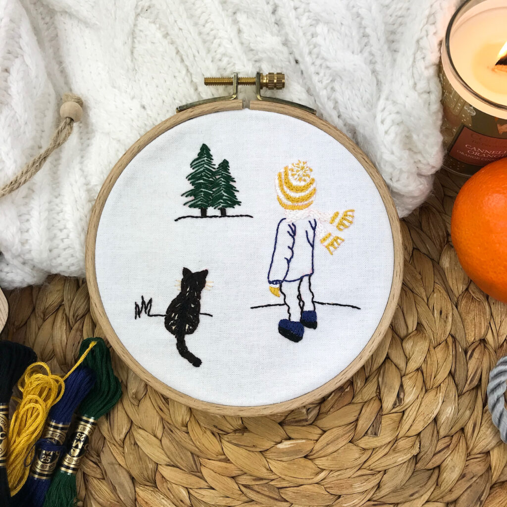 Broderie hivernale sur tambour représentant Clotaire enfant et son chat entourés de sapins