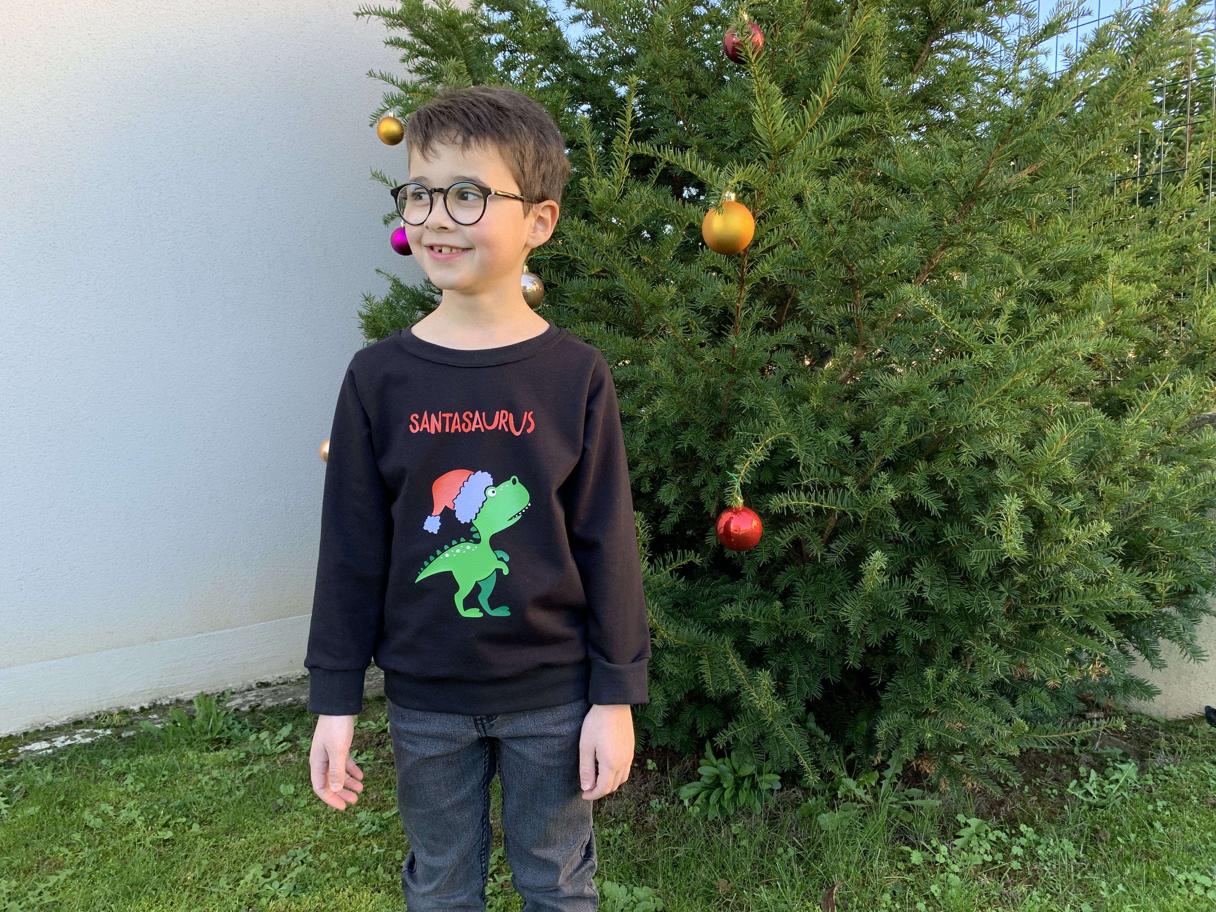 Enfant portant son pull de Noël cousu avec motif dinosaure T-Rex Père Noël en flex thermocollant